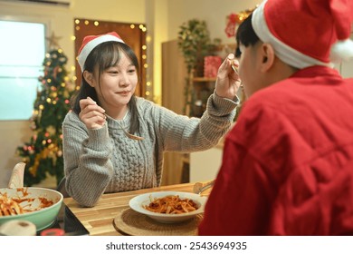 Young couple in Santa hats enjoying a warm holiday dinner in the kitchen decorated with Christmas lights - Powered by Shutterstock