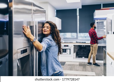 Young couple, satisfied customers choosing fridge in appliances store.