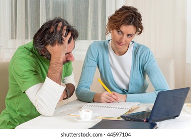 A Young Couple Seated At Their Dining Room Table Contemplating Their Plans For Their Financial Future During This Economic Hardship.