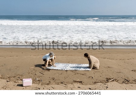 Young couple setting up a patterned beach blanket on a sandy shore. Enjoying a relaxing sunny vacation by the ocean