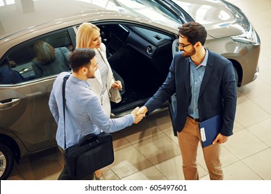 Young Couple Shaking Hands With Sales Agent After A Successful Car Buying