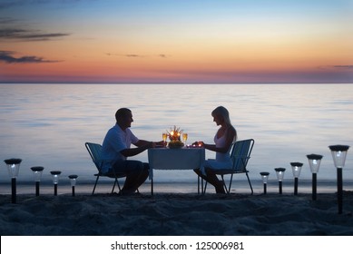 A young couple share a romantic dinner with candles and wine glasses on the sea sand beach