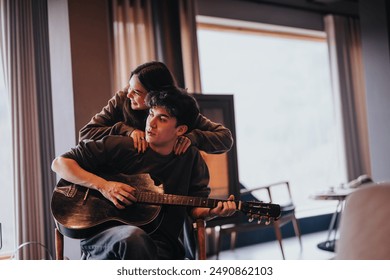 A young couple shares a tender embrace while playing guitar together in a cozy living room setting. - Powered by Shutterstock