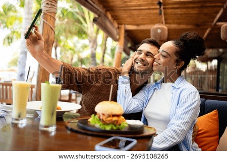 Young couple sharing dining experience at tropical restaurant, engaging with their online followers