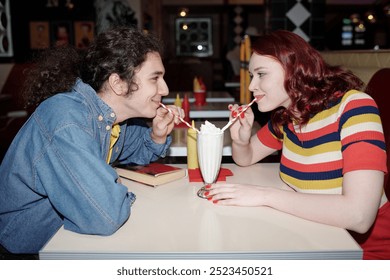 Young couple sharing milkshake at retro-styled diner with colorful decor while sitting across each other engaged in lively conversation - Powered by Shutterstock