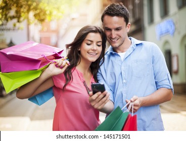 Young Couple With Shopping Bag Using Mobile Phone