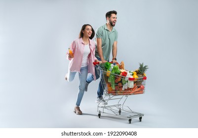 Young couple with shopping cart full of groceries on grey background - Powered by Shutterstock