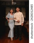 A young couple showcases the beauty of Filipino traditional clothing, with a woman in a Terno and a man in a Barong Tagalog. Full body photo.