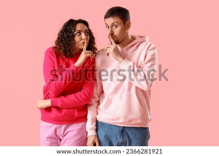 Young couple showing silence gesture on pink background