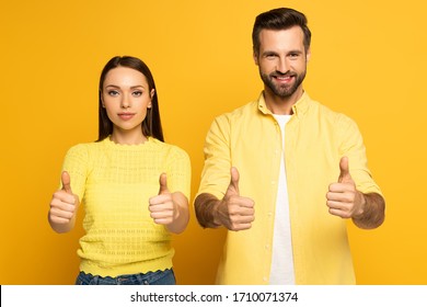 Young Couple Showing Tums Up At Camera On Yellow Background