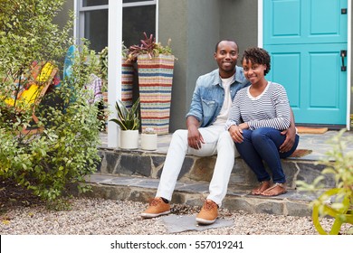 Young couple sit looking to camera outside their new house - Powered by Shutterstock