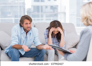 Young couple sit on the couch of the therapist and the woman is crying