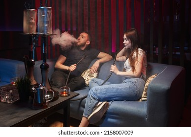 a young couple sits in a hookah lounge on the couch and smokes a hookah, releasing smoke