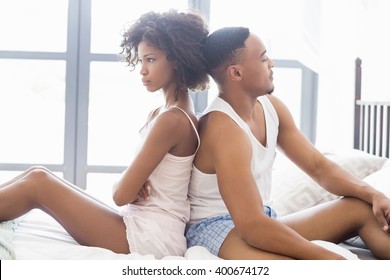 Young couple sitting back to back and ignoring each other in bedroom
