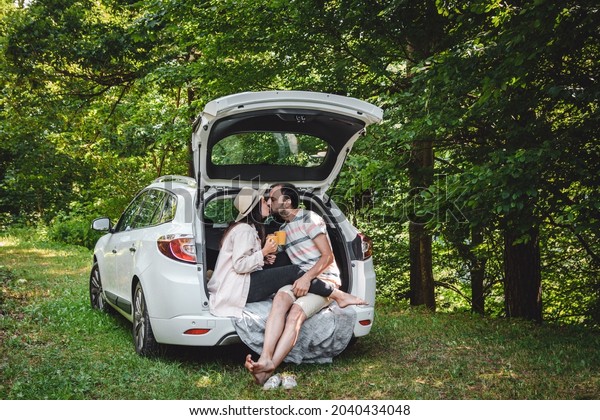 Young couple sitting in boot of car parked in forest,\
drinking coffee 