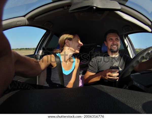A young couple is sitting in\
the cabin of a comfortable modern car. the couple takes a selfie in\
the car. a man is driving. coffee on the way. female\
passenger