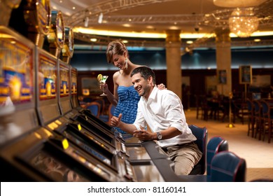 young couple sitting with cocktail, playing the slot machine