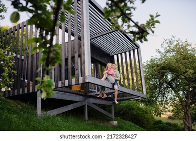 Young couple sitting and cuddling in hammock terrace in their new home in tiny house in woods, sustainable living concept.