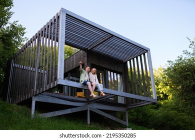 Young couple sitting and cuddling in hammock terrace in their new home in tiny house in woods, sustainable living concept. - Powered by Shutterstock