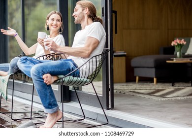 Young couple sitting with cups on the terrace of the modern house talking together outdoors - Powered by Shutterstock