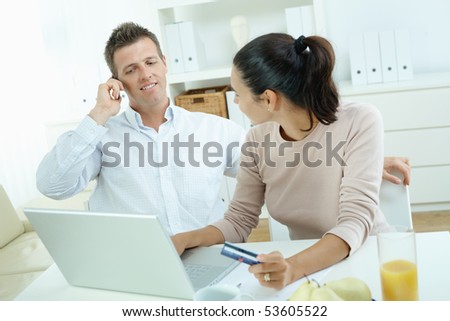Young couple sitting at desk shopping on internet from home. Calling phone, using laptopcomputer and paying with credit card.