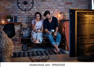 Young Couple Sitting At Home On Pallet Furniture, Watching Tv, Boring Program.