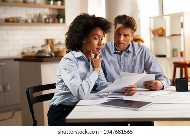 Young couple sitting in the kitchen preparing bills to pay. Stressed woman and man having financial problems
