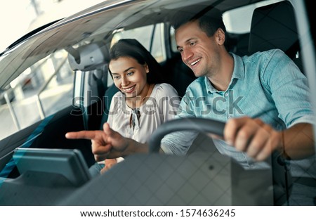 A young couple is sitting in a new car and inspecting it. Buying and renting cars at a car dealership.