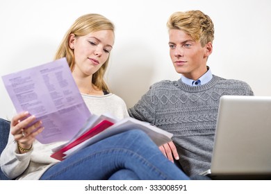 Young Couple Sitting Next To Eachother, Going Through Bills, Invoices And Other Paperwork, Balancing Their Checkbook On A Laptop