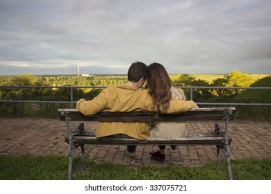 Young Couple Sitting On A Bench, Shot From Behind.