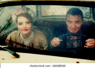 Young Couple Sitting On A Car Window In The Rain