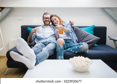 Young Couple Sitting On The Couch, Drinking Coffee And Watching Tv