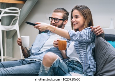 Young Couple Sitting On The Couch, Drinking Coffee And Watching Tv