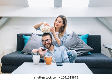 Young Couple Sitting On The Couch, Drinking Coffee And Watching Tv