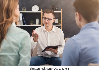 Young Couple Sitting On Couch During Therapy Session, Back View. Therapist Listening And Giving Advices To Married Man And Woman With Relationship Problems, Family Issues Concept, Copy Space