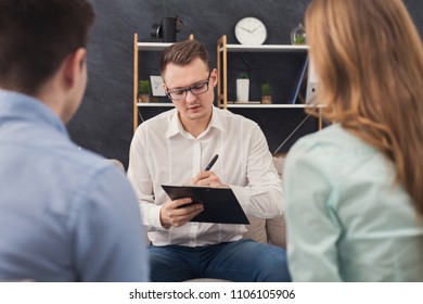 Young Couple Sitting On Couch During Therapy Session, Back View. Therapist Listening And Giving Advices To Married Man And Woman With Relationship Problems, Family Issues Concept, Copy Space