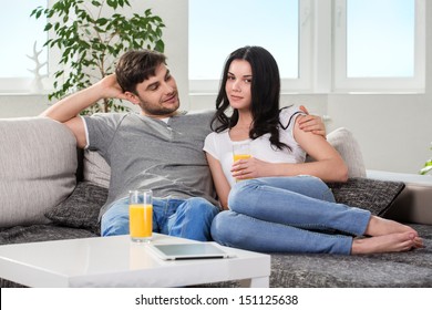 Young Couple Sitting On The Couch, Girl Drinking Orange Juice