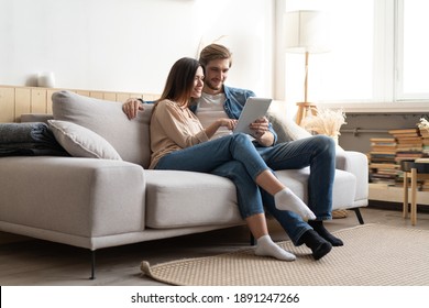 Young couple sitting on couch at home, using a tablet PC for Internet and social media.