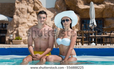 Young couple sitting on the edge of swimming pool at the hotel on a sunny summer day