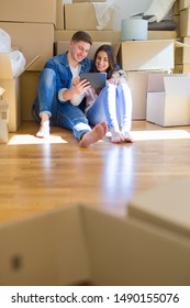Young couple sitting on the floor of new house around cardboard boxes using tablet, smiling happy for new apartment