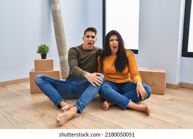 Young Couple Sitting On The Floor At New Home In Shock Face, Looking Skeptical And Sarcastic, Surprised With Open Mouth 