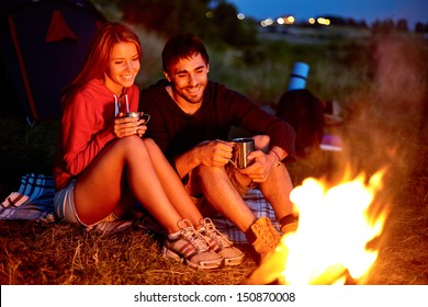 Young couple sitting on the ground and drinking tea while looking at fire