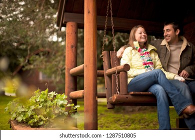 Young couple sitting on a hammock chair on the stoop of a log cabin. - Powered by Shutterstock