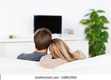 young couple sitting on sofa, watching tv