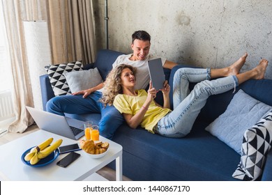 Young Couple Sitting On Sofa At Home Looking In Tablet, Watching Online, Using Internet, Smiling, Happy Together, Having Fun, Man And Woman In Love, Family Leisure Time, Relaxing, Modern Devices