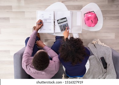 Young Couple Sitting On Sofa Calculating Invoices At Home 