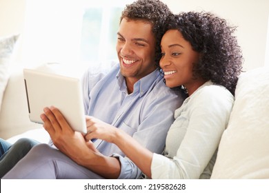 Young Couple Sitting On Sofa Using Digital Tablet - Powered by Shutterstock