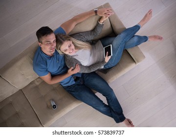 Young Couple Sitting On A Sofa In The Luxury Living Room, Using A Tablet Computer Top View