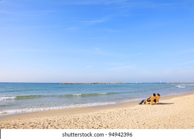 Young couple sitting on Tel-Aviv beach and looking at the sea in a beautiful quiet morning (Mediterranean sea. Israel)