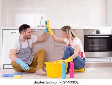 Young couple sitting on tiled floor in kitchen, satisfied after finished chores, Teamwork in housework - Powered by Shutterstock